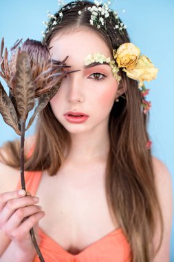 Kozmetik ve manikür. Yakın çekim portre olan kuru çiçekler onun yüz ve saç, pastel renkli, çekici kadın makyaj mükemmel ve mavi arka plan üzerinde deri. Taze, trendy, Bahar düzeltisiz portre