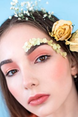 Kozmetik ve manikür. Yakın çekim portre olan kuru çiçekler onun yüz ve saç, pastel renkli, çekici kadın makyaj mükemmel ve mavi arka plan üzerinde deri. Taze, trendy, Bahar düzeltisiz portre