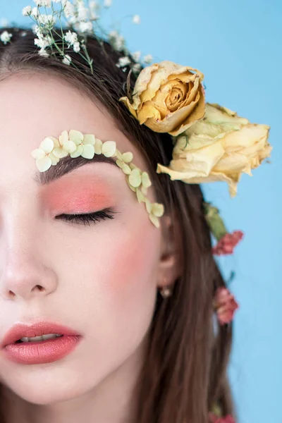 Cosméticos y manicura. Retrato de cerca de una mujer atractiva con flores secas en la cara y el cabello, color pastel, maquillaje perfecto y piel sobre fondo azul. Retrato retocado de primavera fresco, moderno — Foto de Stock