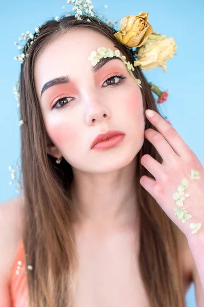 Cosméticos e manicure. Retrato close-up de mulher atraente com flores secas em seu rosto e cabelo, cor pastel, maquiagem perfeita e pele no fundo azul. Retrato retocado de primavera fresco, na moda — Fotografia de Stock