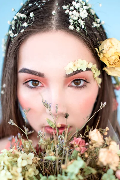 Cosméticos e manicure. Retrato close-up de mulher atraente com flores secas em seu rosto e cabelo, cor pastel, maquiagem perfeita e pele no fundo azul. Retrato retocado de primavera fresco, na moda — Fotografia de Stock