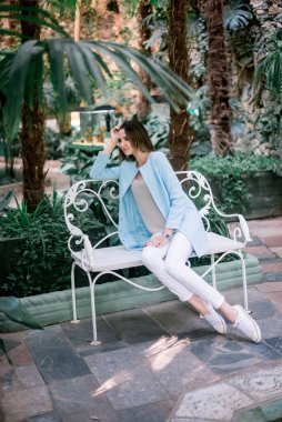 Genç, zarif, pozitif kız botanik bahçesinde mavi ceketli poz veriyor..