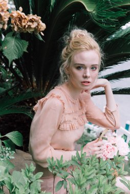 Şehvetli genç sarışın güzel ve zarif bir kadın kayaya oturmuş Çin 'deki tropik yeşil orman palmiyesinden kameraya bakıyor..