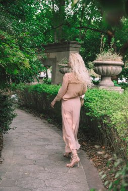 Şehvetli genç sarışın güzel ve zarif bir kadın kayaya oturmuş Çin 'deki tropik yeşil orman palmiyesinden kameraya bakıyor..