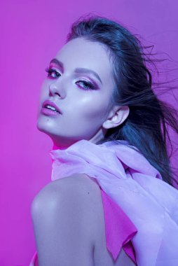Pembe kurdeleli uzun kıvırcık saçlı güzel, modaya uygun bir kız. Stüdyodaki pembe arka plandaki kız. Moda, güzellik. Parlak kıyafetler. Saç için makyaj malzemeleri, sağlıklı saçlar..