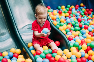 Gülen çocuk 1-2 yaşında, çocuk parkında ve oyun merkezinde doğum günü partisinde top havuzunda eğleniyor. Çocuk oyun parkında renkli toplarla oynuyor. Küçük çocuk için oyuncaklar.