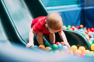 Gülen çocuk 1-2 yaşında, çocuk parkında ve oyun merkezinde doğum günü partisinde top havuzunda eğleniyor. Çocuk oyun parkında renkli toplarla oynuyor. Küçük çocuk için oyuncaklar.