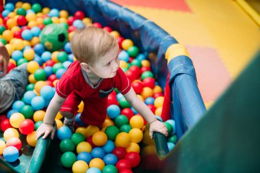 Gülen çocuk 1-2 yaşında, çocuk parkında ve oyun merkezinde doğum günü partisinde top havuzunda eğleniyor. Çocuk oyun parkında renkli toplarla oynuyor. Küçük çocuk için oyuncaklar.