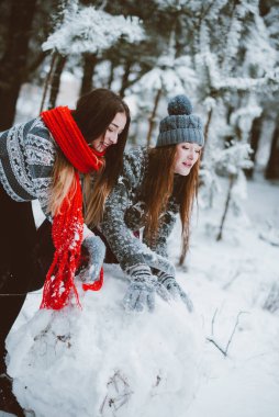 İki genç yeniyetme kız arkadaş bir arada. İki kız kardeşin moda portresini yakın çekin. Kışları eğlenin, süveter giyin, en iyi arkadaşlar açık havada, karlı havada.