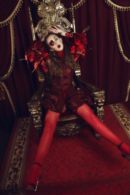 Kupa kızı gibi giyinmiş bir kadın, büyük bir yüreği olan yaratıcı bir makyaj, tahtta oturan bir kız, son rötuşlu bir portre. Kavramsal fotoğraf