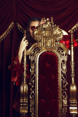 Kupa kızı gibi giyinmiş bir kadın, büyük bir yüreği olan yaratıcı bir makyaj, tahtta oturan bir kız, son rötuşlu bir portre. Kavramsal fotoğraf