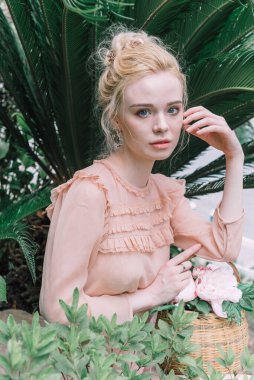 Şehvetli genç sarışın güzel ve zarif bir kadın kayaya oturmuş Çin 'deki tropik yeşil orman palmiyesinden kameraya bakıyor..