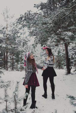 İki genç yeniyetme kız arkadaş bir arada. İki kız kardeşin moda portresini yakın çekin. Kışları eğlenin, süveter giyin, en iyi arkadaşlar açık havada, karlı havada.