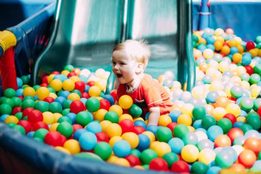 Gülen çocuk 1-2 yaşında, çocuk parkında ve oyun merkezinde doğum günü partisinde top havuzunda eğleniyor. Çocuk oyun parkında renkli toplarla oynuyor. Küçük çocuk için oyuncaklar.