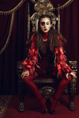 Kupa kızı gibi giyinmiş bir kadın, büyük bir yüreği olan yaratıcı bir makyaj, tahtta oturan bir kız, son rötuşlu bir portre. Kavramsal fotoğraf