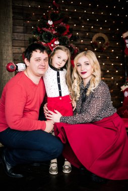 Kırmızılı güzel bir aile Noel tatili için birlikte eğleniyor, oturma odasında yerde oturuyor, güzel dekore edilmiş bir Noel ağacının yanında, gülümsüyor.
