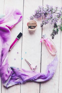 Düz yatıyordu, üst görünüm yaylı masa çerçevesi. Ahşap zemin üzerinde kozmetik, ruj ve leylak çiçekleri olan kadınsı masa çalışma alanı.