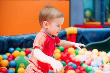 Gülen çocuk 1-2 yaşında, çocuk parkında ve oyun merkezinde doğum günü partisinde top havuzunda eğleniyor. Çocuk oyun parkında renkli toplarla oynuyor. Küçük çocuk için oyuncaklar.