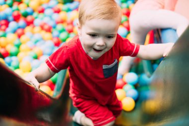 Gülen çocuk 1-2 yaşında, çocuk parkında ve oyun merkezinde doğum günü partisinde top havuzunda eğleniyor. Çocuk oyun parkında renkli toplarla oynuyor. Küçük çocuk için oyuncaklar.