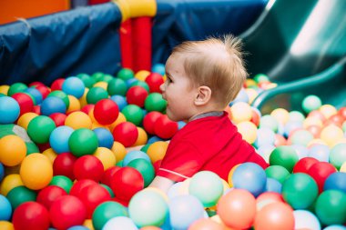 Gülen çocuk 1-2 yaşında, çocuk parkında ve oyun merkezinde doğum günü partisinde top havuzunda eğleniyor. Çocuk oyun parkında renkli toplarla oynuyor. Küçük çocuk için oyuncaklar.