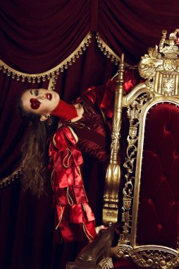 Kupa kızı gibi giyinmiş bir kadın, büyük bir yüreği olan yaratıcı bir makyaj, tahtta oturan bir kız, son rötuşlu bir portre. Kavramsal fotoğraf