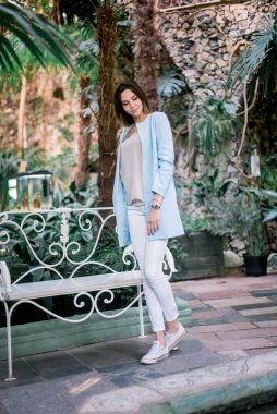 Genç, zarif, pozitif kız botanik bahçesinde mavi ceketli poz veriyor..