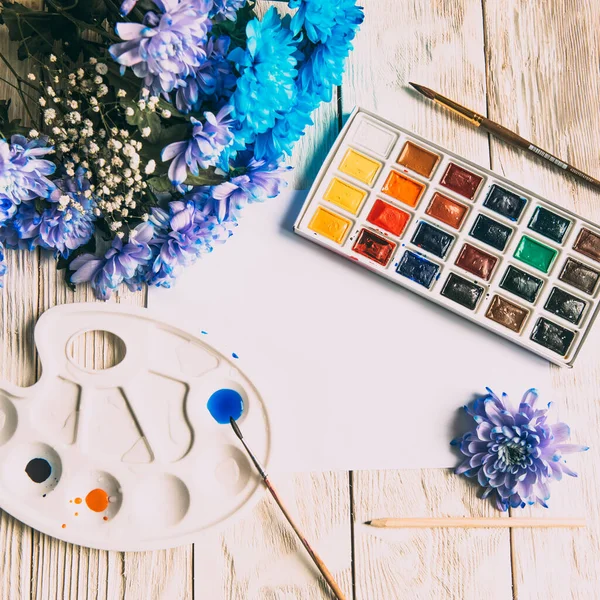 Palette of watercolor paints, brushes and paper for a water color on wooden background, close up. Flat lay, spring background with copy space.