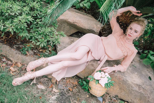 在中国 年轻性感的金发美女穿着粉色的衣服坐在岩石上 凝视着热带绿色丛林棕榈背景上的相机 — 图库照片