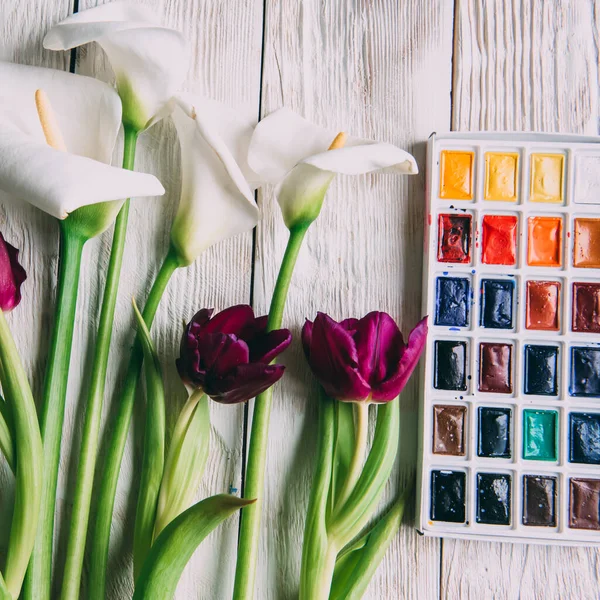 Palette of watercolor paints, brushes and paper for a water color on wooden background, close up. Flat lay, spring background with copy space.