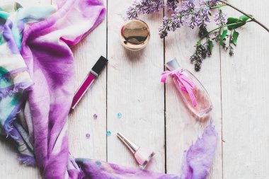 Düz yatıyordu, üst görünüm yaylı masa çerçevesi. Ahşap zemin üzerinde kozmetik, ruj ve leylak çiçekleri olan kadınsı masa çalışma alanı.