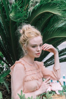 Şehvetli genç sarışın güzel ve zarif bir kadın kayaya oturmuş Çin 'deki tropik yeşil orman palmiyesinden kameraya bakıyor..