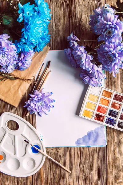 Palette of watercolor paints, brushes and paper for a water color on wooden background, close up. Flat lay, spring background with copy space.