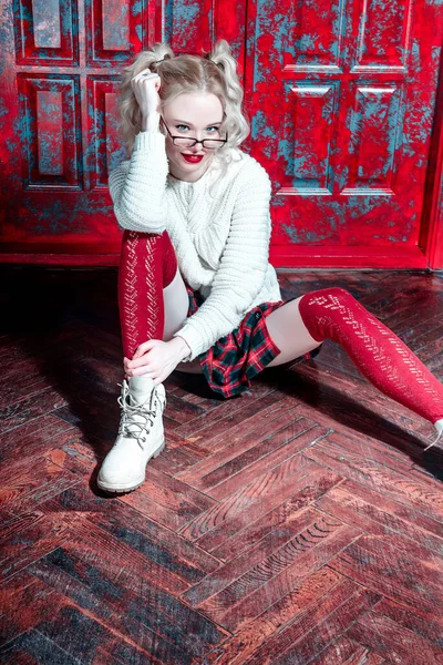 Fashion shot of a blonde girl wearing modern youth clothes. College, school style. Hipster girl wearing glasses by a brick wall. Youth fashion