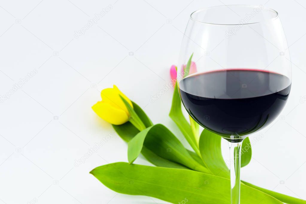 Studio photography with a glass of red white in front of yellow and pink-orange tulips isolated on white background creating an romantic and festive atmosphere.