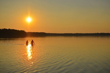 Gölün üzerinde güzel, ılık gün batımı. Suda insan siluetleri var.