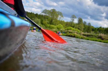 Back view of a hand with red paddle kayaking on the river, concept of spring water sports. Selective focus.