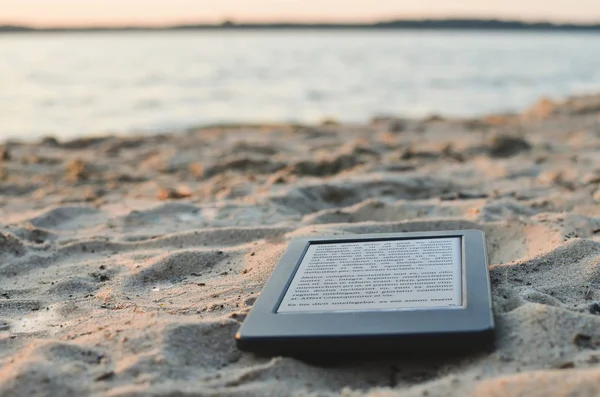 E-book reader laying on the beach sand. Lorem ipsum text used