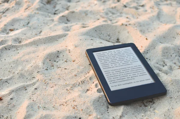 E-book reader laying on the beach sand. Lorem ipsum text used