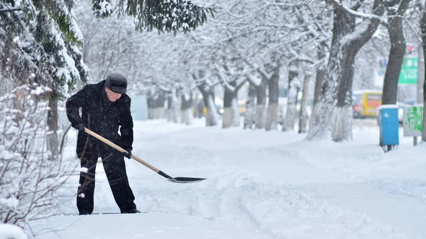 Man is cleaning city street from snow at heavy snowfall in winter.