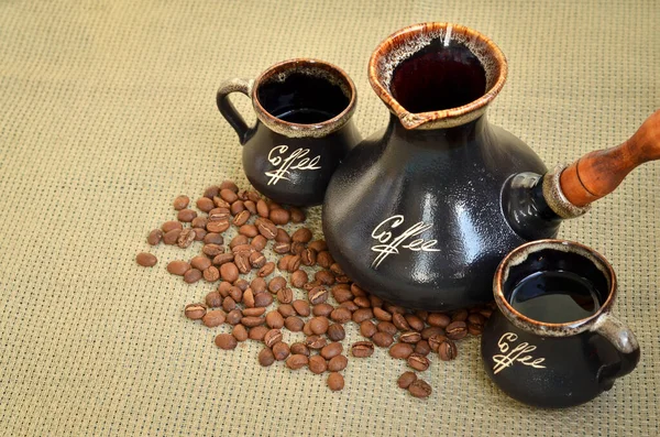 Coffee cezve with two cups and spilled coffee beans on sackcloth background. Selective focus.