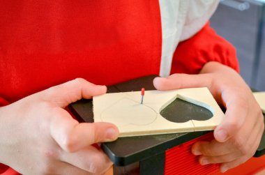 Boy is learning woodworking with a wood-crafting machine tool. Cutting a DIY wooden heart with a jigsaw. Selective focus.