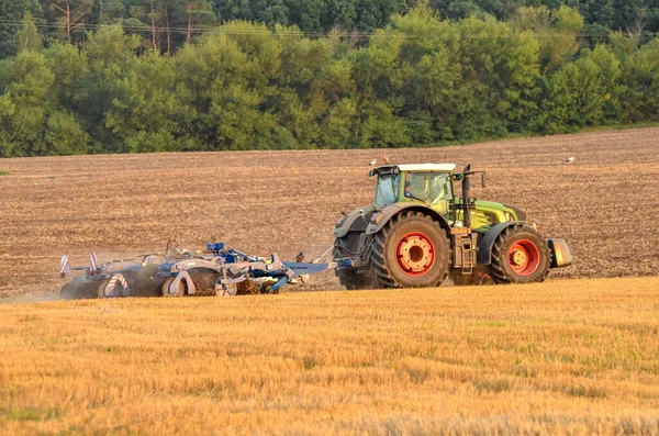 Tractor working on field after harvesting at sunset.