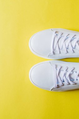 Bir çift parlak sarı arka planda beyaz deri spor ayakkabı. Boşluğu kopyala.