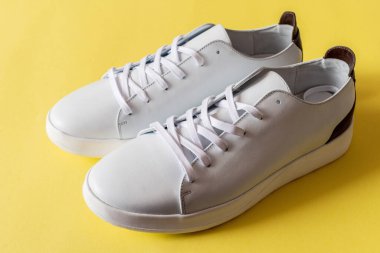 Bir çift parlak sarı arka planda beyaz deri spor ayakkabı. Boşluğu kopyala.