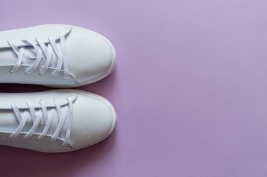 Canlı mor arka planda bir çift beyaz deri spor ayakkabı. Boşluğu kopyala.