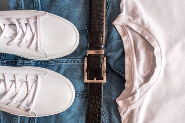 Beyaz deri spor ayakkabıları, kemer, kot pantolon ve beyaz tişört karışımı..