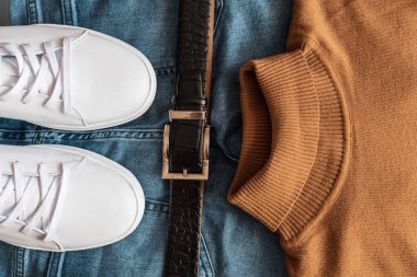 Düz deri spor ayakkabılar, siyah kuşak, mavi kot pantolon ve bej kazak..