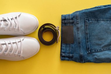 Sarı arka planda beyaz spor ayakkabılar ve mavi kot pantolon..