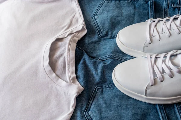 Combination of white leather sneakers, blue jeans and white t-shirt, Top view.