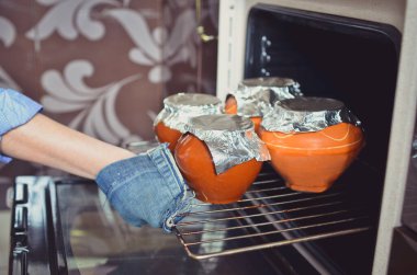 Kahverengi seramik kaplarda pişmiş ya da yahni tatmış bir kadın fırından çıkarken. Düşük Dof. Üst görünüm.